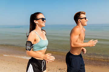 Image showing couple with phones and arm bands running on beach