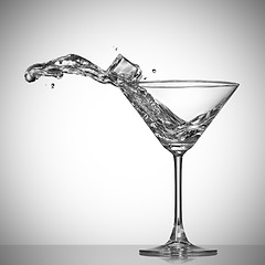 Image showing Clear cocktail splash out of glass with ice cube.