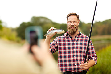 Image showing friend photographing fisherman with fish at lake