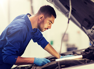 Image showing mechanic man with lamp repairing car at workshop