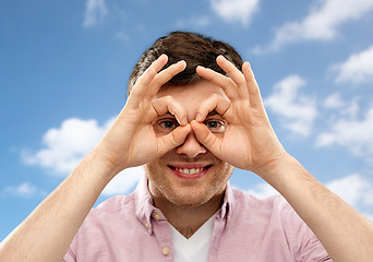 Image showing young man looking through finger glasses over sky