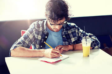 Image showing man with notebook and juice writing at cafe