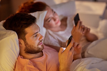 Image showing couple using smartphones in bed at night