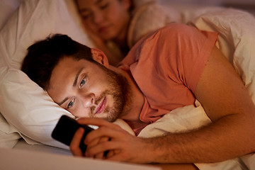 Image showing man using smartphone while girlfriend is sleeping