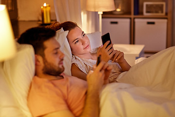 Image showing couple using smartphones in bed at night