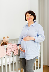 Image showing happy pregnant woman next to baby bed at home