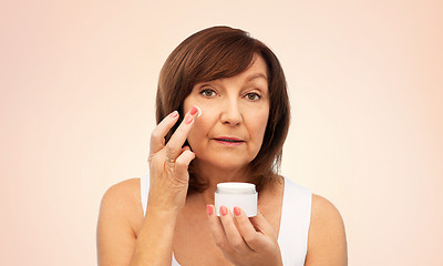 Image showing senior woman applying cream to her face