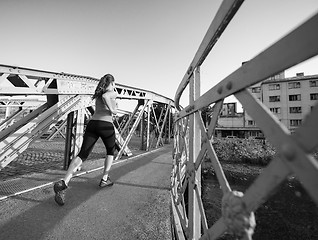 Image showing woman jogging across the bridge at sunny morning