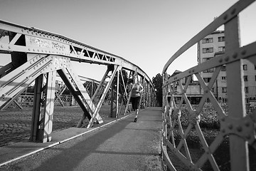 Image showing woman jogging across the bridge at sunny morning