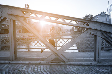 Image showing woman jogging across the bridge at sunny morning