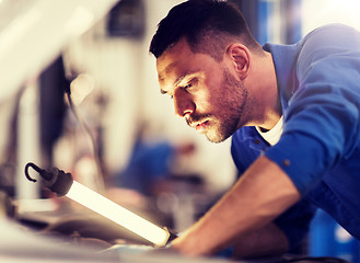 Image showing mechanic man with lamp repairing car at workshop