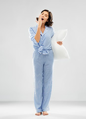 Image showing sleepy woman in pajama holding pillow and yawning