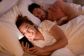 Image showing woman using smartphone while boyfriend is sleeping