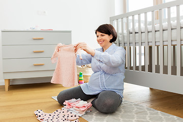 Image showing happy pregnant woman setting baby clothes at home