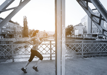 Image showing woman jogging across the bridge at sunny morning