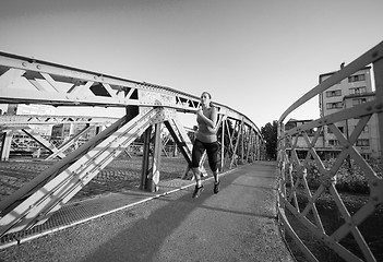 Image showing woman jogging across the bridge at sunny morning