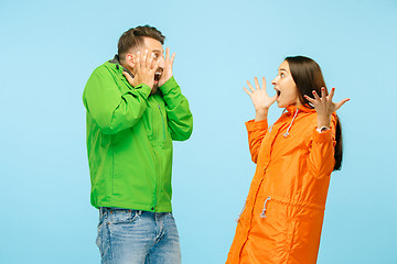 Image showing The young surprised couplel posing at studio in autumn jackets isolated on blue