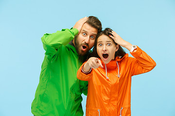 Image showing The young surprised couplel posing at studio in autumn jackets isolated on blue