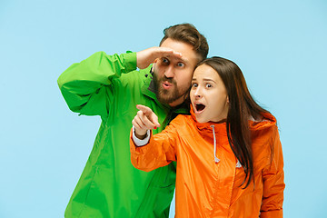 Image showing The young surprised couplel posing at studio in autumn jackets isolated on blue