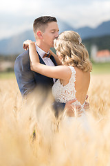 Image showing Groom hugging bride tenderly and kisses her on forehead in wheat field somewhere in Slovenian countryside.