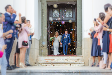 Image showing Newlyweds exiting the church after the wedding ceremony, family and friends celebrating their love with the shower of soap bubbles, custom undermining traditional rice bath