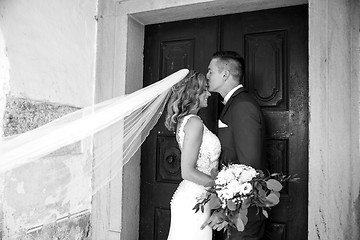 Image showing The kiss. Groom kisses bride on forehead in front of church portal.