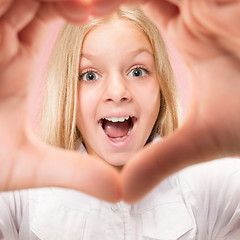Image showing Beautiful smiling teen girl makes the shape of a heart with her hands on the pink background.