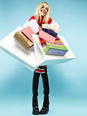 Image showing Full length portrait of a beautiful smiling woman walking with colorful shopping bags isolated over blue background