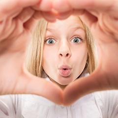 Image showing Beautiful smiling teen girl makes the shape of a heart with her hands on the pink background.