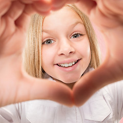 Image showing Beautiful smiling teen girl makes the shape of a heart with her hands on the pink background.