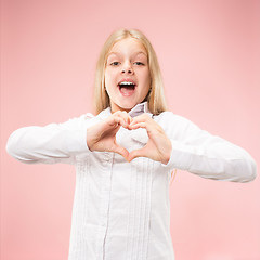 Image showing Beautiful smiling teen girl makes the shape of a heart with her hands on the pink background.