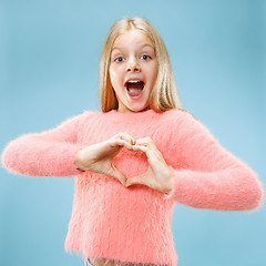 Image showing Beautiful smiling teen girl makes the shape of a heart with her hands on the blue background.