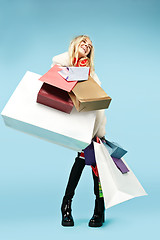 Image showing Full length portrait of a beautiful smiling woman walking with colorful shopping bags isolated over blue background