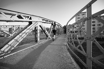 Image showing woman jogging across the bridge at sunny morning