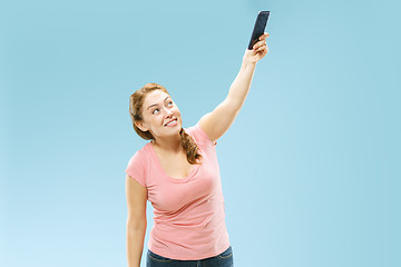 Image showing Portrait of a happy smiling casual girl showing blank screen mobile phone isolated over blue background