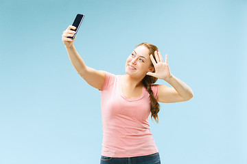 Image showing Portrait of a happy smiling casual girl showing blank screen mobile phone isolated over blue background