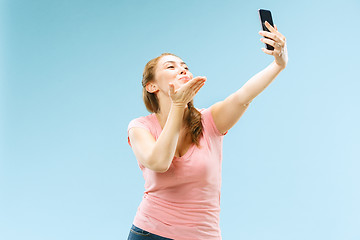 Image showing Portrait of a happy smiling casual girl showing blank screen mobile phone isolated over blue background