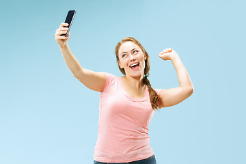 Image showing Portrait of a happy smiling casual girl showing blank screen mobile phone isolated over blue background