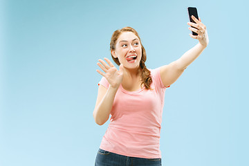 Image showing Portrait of a happy smiling casual girl showing blank screen mobile phone isolated over blue background