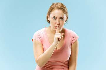 Image showing The young woman whispering a secret behind her hand over blue background