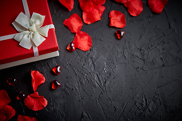 Image showing Gift box on black stone table. Romantic holiday background with rose petals