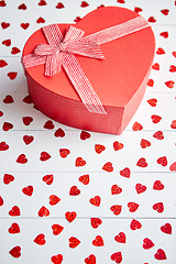 Image showing Boxed gift placed on heart shaped red sequins on white wooden table