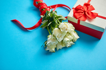 Image showing Bouquet of white roses with red bow on blue background. Boxed gift on side