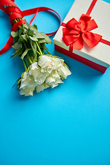 Image showing Bouquet of white roses with red bow on blue background. Boxed gift on side