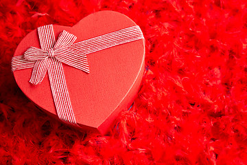 Image showing Heart shaped boxed gift, placed on red feathers background