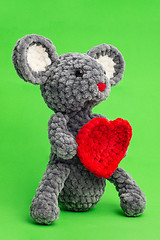 Image showing Grey knitted mouse with a heart in hand on a green background, side view