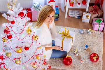 Image showing Young girl at the Christmas tree with a gift in her hands