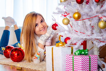 Image showing A young girl lies at the Christmas tree and looks happy in the frame