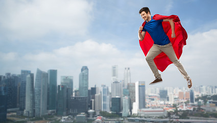 Image showing man in red superhero cape flying in air over city