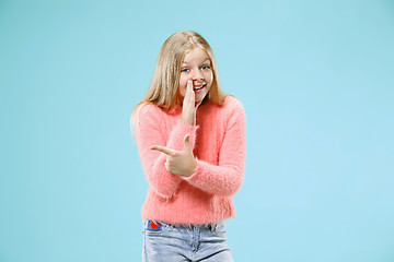 Image showing The young teen girl whispering a secret behind her hand over blue background